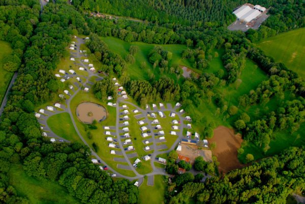 An aerial photograph of Lodge Coppice. Well spaced caravans, trees and the pool all seen from above.