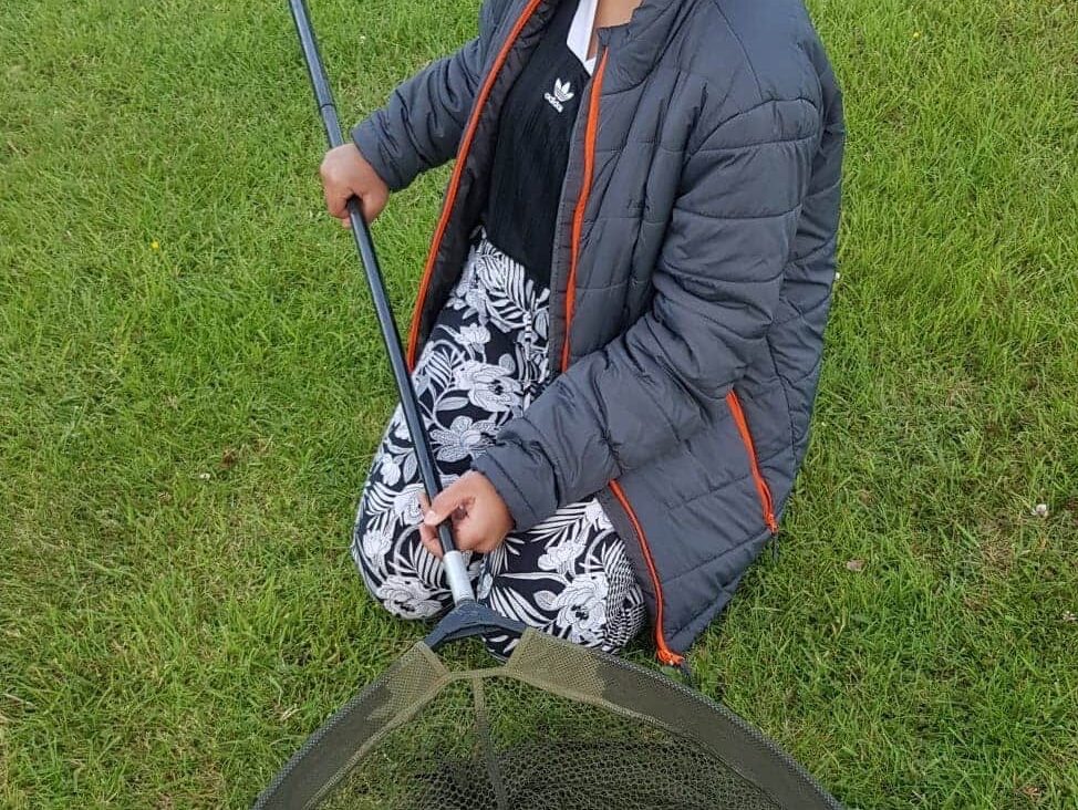 A young fishing girl showing a big fish in her keep net.