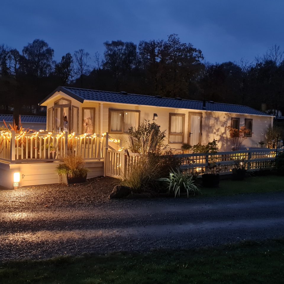 View of a lodge coppice static caravan illuminated with at night with external decking and balustrade lights