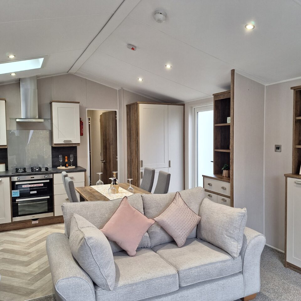 A twin sofa in the foreground of an open plan static caravan at Lodge Coppice with kithen behind