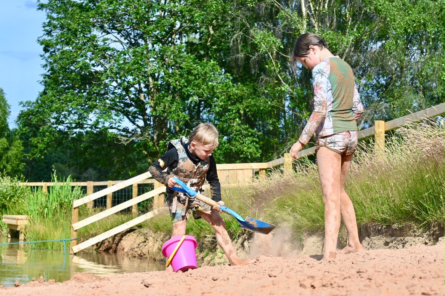 a56ad393-46f2-430c-b175-e8d695bc24ab Youngsters playing with bucket and spade on beach area next to non-motorised water sports lake